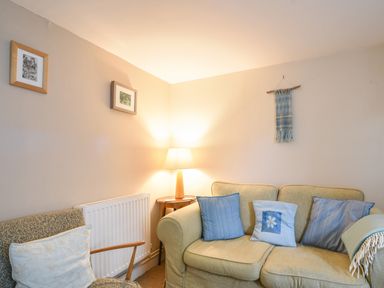 A living room with a beige sofa with blue cushions a patterned armchair and a lamp on a side table at 30 Sherborne Lane in Lyme Regis