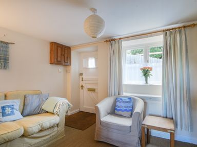 A small living room with a beige sofa and armchair a wooden side table and a window with flowers on the sill at 30 Sherborne Lane in Lyme Regis