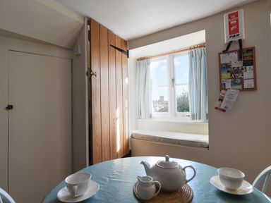 A small dining area with a round table set with a teapot cups and a milk jug near a window with curtains and a wooden door at 30 Sherborne Lane Lyme Regis