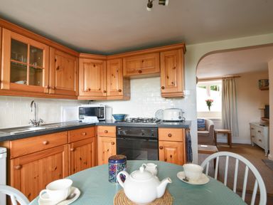 A kitchen with wooden cabinets a round table with a teapot and cups and a view of a living room at 30 Sherborne Lane Lyme Regis