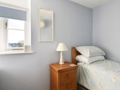 A bedroom with a bed a wooden nightstand a lamp a window with a blue blind and a rectangular mirror on the wall at 30 Sherborne Lane Lyme Regis