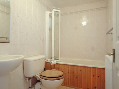 A bathroom with a toilet that has a wooden seat a bathtub with a wooden panel and a shower screen at 30 Sherborne Lane Lyme Regis