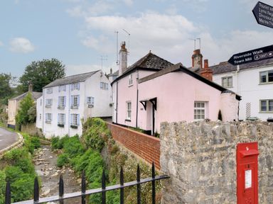 A stone and brick wall with a red post box and houses next to a small stream at 30 Sherborne Lane in Lyme Regis