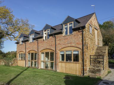 A two story stone and brick house with multiple windows and an exterior stone staircase with a lawn at The Granary in Little Dasset near Gaydon