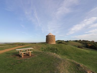 A picnic table on grassy hills with a small round stone tower under a clear sky at The Granary in Little Dasset near Gaydon