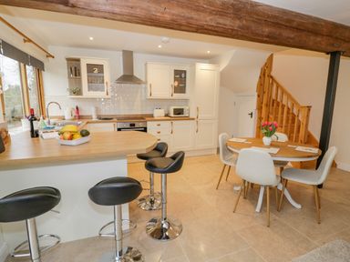 A kitchen with an island countertop with three bar stools and a dining table with four chairs and flowers at The Granary Little Dasset near Gaydon