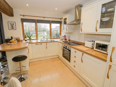 A kitchen with white cabinets wooden countertops a stovetop oven microwave toaster sink and bar stools at The Granary Little Dasset near Gaydon
