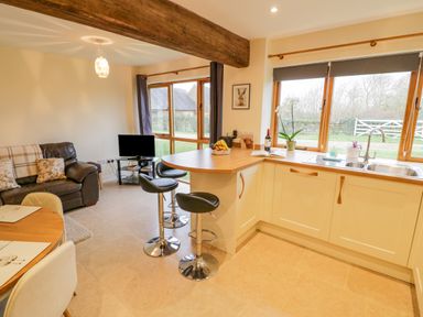 A kitchen with bar stools and a sink next to a living area with a sofa and television at The Granary Little Dasset near Gaydon