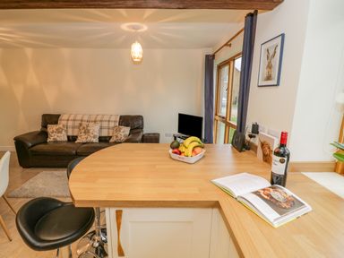 A kitchen counter with fruit bowl and wine bottle near a living room with sofa and small TV at The Granary in Little Dasset near Gaydon
