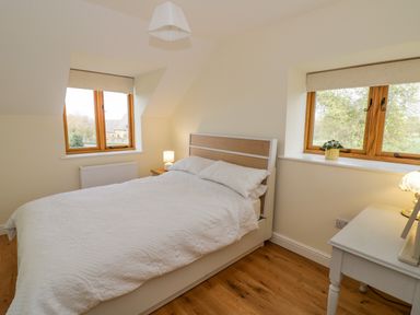 A bedroom with a double bed white bedding wooden floor bedside tables lamps and two windows at The Granary in Little Dasset near Gaydon