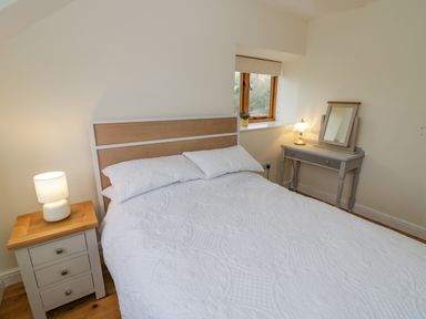 A bedroom with a double bed bedside table with lamp and dressing table with mirror at The Granary in Little Dasset near Gaydon