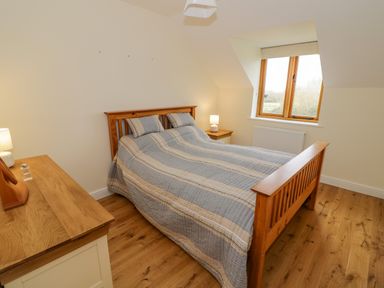 A bedroom with a wooden bed and bedside tables with lamps and a window at The Granary Little Dasset near Gaydon