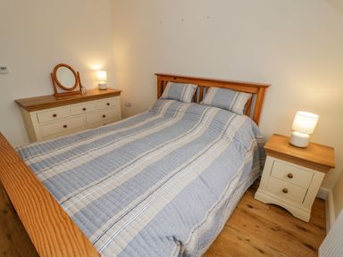 A bedroom with a double bed pillows bedside table with lamp and dresser with mirror at The Granary Little Dasset near Gaydon