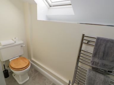 A bathroom with a toilet with a wooden seat a towel rail with towels and a skylight window at The Granary in Little Dasset near Gaydon