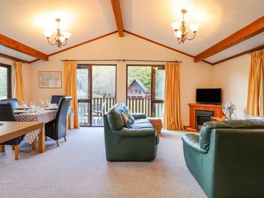 A living room with green leather sofas a dining table with chairs and large windows overlooking a garden at Dartmoor Retreat Lodge in Clifford Bridge near Moretonhampstead