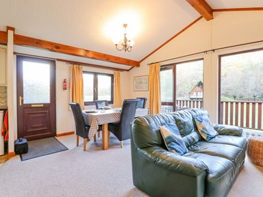 A living room with a green leather sofa, dining table with black chairs, and large windows at Dartmoor Retreat Lodge Clifford Bridge near Moretonhampstead