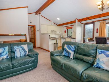 A living room with green leather sofas and blue patterned cushions next to a kitchen and dining area at Dartmoor Retreat Lodge Clifford Bridge near Moretonhampstead