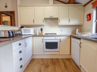 A kitchen with cream cabinets a white oven a microwave toaster and dishwasher at Dartmoor Retreat Lodge Clifford Bridge near Moretonhampstead