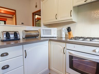 A kitchen countertop with a toaster bread bin microwave and knife block beside a gas stove at Dartmoor Retreat Lodge Clifford Bridge near Moretonhampstead