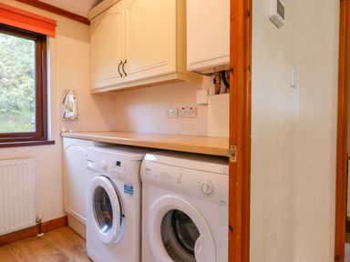 A laundry room with two white front-loading machines under a countertop and cabinets above at Dartmoor Retreat Lodge Clifford Bridge near Moretonhampstead