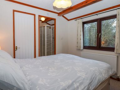 A bedroom with a bed window curtains a radiator door and an en suite shower at Dartmoor Retreat Lodge Clifford Bridge near Moretonhampstead