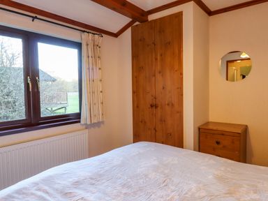 A bedroom with a bed a wooden wardrobe a small wooden chest of drawers and a window with curtains at Dartmoor Retreat Lodge Clifford Bridge near Moretonhampstead