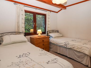 A bedroom with two single beds a wooden chest of drawers and a window with curtains at Dartmoor Retreat Lodge Clifford Bridge near Moretonhampstead