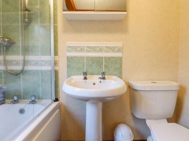 A bathroom with a bathtub shower combination a pedestal sink a toilet and a small trash bin at Dartmoor Retreat Lodge in Clifford Bridge near Moretonhampstead