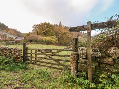 A wooden gate beside a stone wall with two wooden signposts in a grassy rural area at Dartmoor Retreat Lodge Clifford Bridge near Moretonhampstead