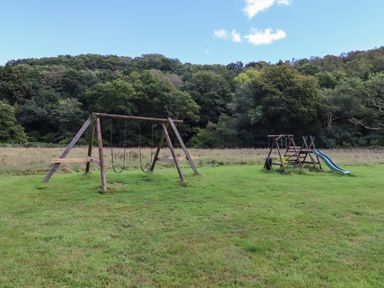 A playground with swings and a slide on a grass field near a forest at Dartmoor Retreat Lodge in Clifford Bridge near Moretonhampstead