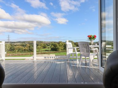 A patio with white chairs and a table with flowers overlooking a green landscape at Chestnut Lodge in Teigngrace near Newton Abbot
