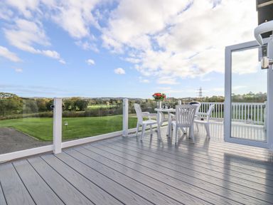 A deck with white chairs and a table overlooking a green lawn and countryside at Chestnut Lodge in Teigngrace near Newton Abbot