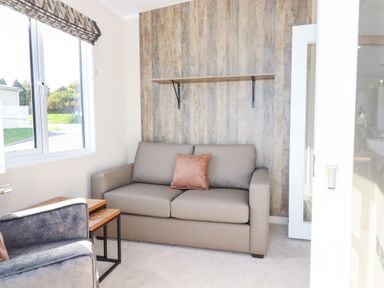 A small living room with a gray sofa and single orange pillow a gray armchair two nested wooden tables and a window at Chestnut Lodge in Teigngrace near Newton Abbot