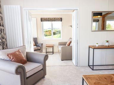 A living room with armchairs, sofas, a wooden table, a console table with plants, and a window at Chestnut Lodge in Teigngrace near Newton Abbot