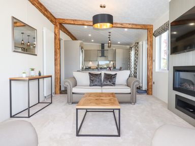 A living room with a sofa coffee table and fireplace overlooking a kitchen with wooden beams at Chestnut Lodge in Teigngrace near Newton Abbot