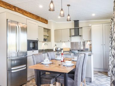 A kitchen with a stainless steel refrigerator and a wooden dining table set with plates bowls and glasses at Chestnut Lodge in Teigngrace near Newton Abbot