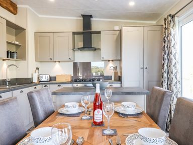 A kitchen and dining area with set table and chairs and a bottle on the table at Chestnut Lodge in Teigngrace near Newton Abbot