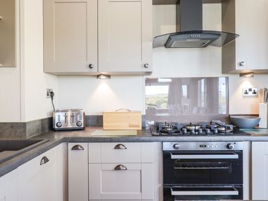 A kitchen with a toaster bread box gas stove oven and cabinets at Chestnut Lodge in Teigngrace near Newton Abbot