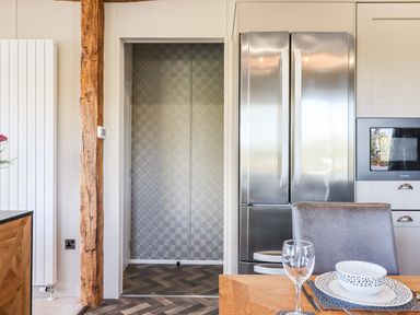 A kitchen area with a stainless steel refrigerator microwave a wooden dining table with a chair and a patterned bowl at Chestnut Lodge in Teigngrace near Newton Abbot