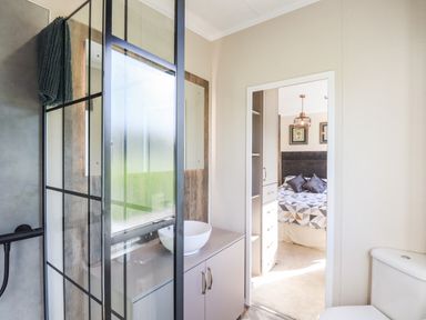 A bathroom with a glass shower enclosure a white sink on a countertop and a toilet next to a doorway leading to a bedroom at Chestnut Lodge in Teigngrace near Newton Abbot