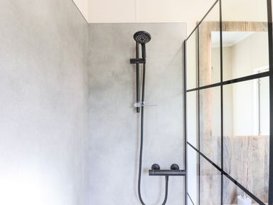 A shower area with a black showerhead and handle against light grey tiled walls with a black-framed glass partition in a bathroom at Chestnut Lodge in Teigngrace near Newton Abbot