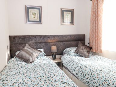 A bedroom with two single beds with patterned bedding a lamp between the beds and framed pictures on the wall at Chestnut Lodge in Teigngrace near Newton Abbot