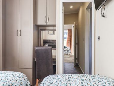 A bedroom with two beds in the foreground a wardrobe and desk with chair on the left and a doorway showing another bedroom at Chestnut Lodge in Teigngrace near Newton Abbot