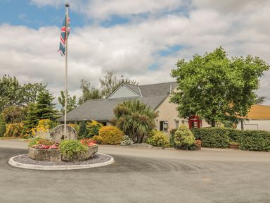 A roundabout with a flagpole and flowers in front of a building surrounded by trees and bushes at Chestnut Lodge in Teigngrace near Newton Abbot