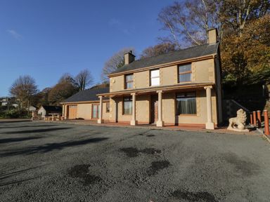 A two-story house with beige walls and columns in front of the entrance surrounded by trees at Bryn Berthen in Penrhyndeudraeth