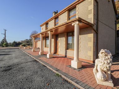 Exterior of a house with columns and lion statues on a paved area at Bryn Berthen in Penrhyndeudraeth