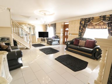 A living room with black leather sofas black rugs a television and ornate curtains at Bryn Berthen in Penrhyndeudraeth