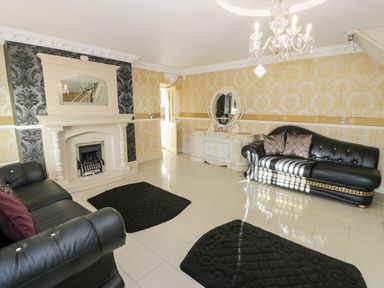 A living room with black leather sofas a fireplace mirror chandelier and rugs at Bryn Berthen in Penrhyndeudraeth