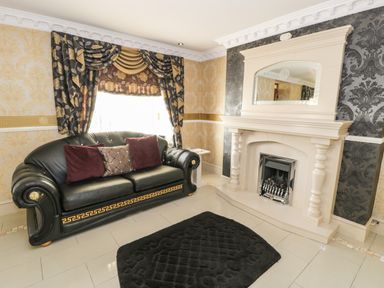 A living room with a black leather sofa with cushions a fireplace and patterned curtains at Bryn Berthen in Penrhyndeudraeth