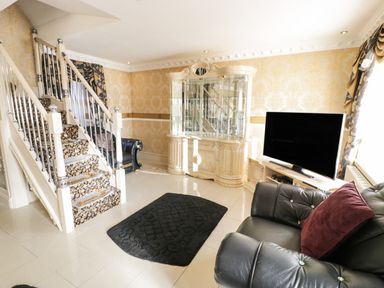 A living room with black leather sofas a large TV on a stand a glass display cabinet and a staircase with patterned carpet at Bryn Berthen in Penrhyndeudraeth